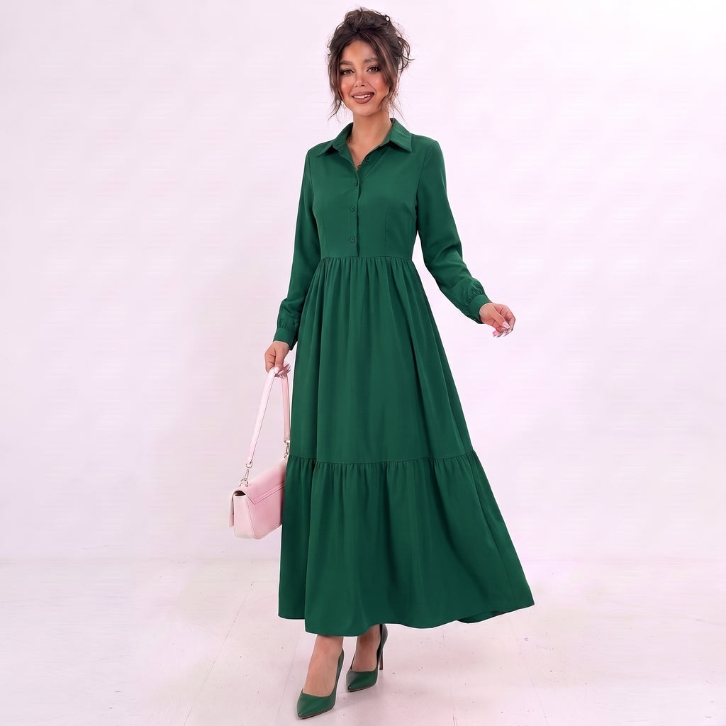 A woman modeling a long-sleeve green collared maxi dress with a tiered skirt, holding a light pink handbag and wearing green pointed-toe heels against a plain light background.