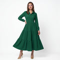 A woman modeling a long-sleeve green midi dress with a tiered skirt and buttoned collar, standing against a plain white studio background.