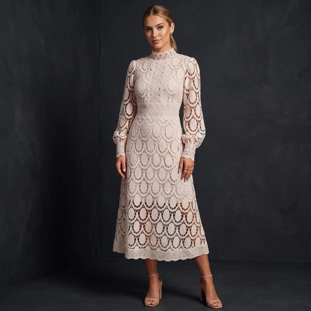 A woman stands against a dark studio backdrop wearing a long-sleeve lace midi dress in a warm off-white/cream tone with a scalloped openwork pattern. The dress has a fitted waist and a slightly flared hem, paired with nude high-heel sandals.